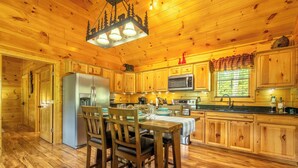 A wooden cabin interior with a dining table, chairs, a refrigerator, a microwave, and wooden cabinets.