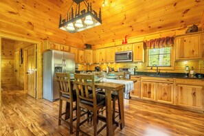 A wooden cabin interior with a dining table, chairs, a refrigerator, a microwave, and wooden cabinets. - Hilltop Hideaway - Relax, Rewind and Renew (Gatlinburg)