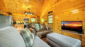A cozy cabin interior with a wooden interior, a leather sofa, a television, and a kitchen area.