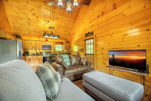 A cozy cabin interior with a wooden interior, a leather sofa, a television, and a kitchen area. - Hilltop Hideaway - Relax, Rewind and Renew (Gatlinburg)