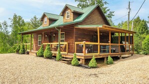 A log cabin with a porch, multiple windows, and a green roof.