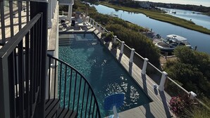 Piscina com espreguiçadeiras, vista para a água e a costa distante.