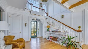 Ein geräumiges Foyer mit hoher Decke, einer Holztreppe und Blick ins Freie.