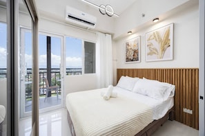 A modern bedroom with a large bed, a view of the city, and artwork on the wall. - Elegant Wood-accent Studio With Balcony (Lapu-Lapu)
