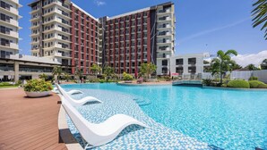 Un hotel moderno con una piscina grande, varios pisos y un cielo azul despejado.