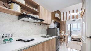 Una cocina moderna con armarios de madera, encimera blanca y electrodomésticos de acero inoxidable. Se ve un comedor con una mesa y sillas a través de una puerta abierta.
