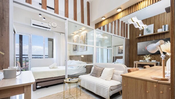 Un dormitorio moderno con un ventanal grande, una cama, un sofá, un escritorio y un televisor.
