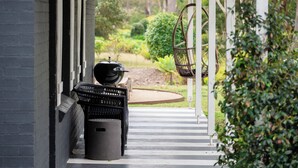 A covered porch with a grill, a hanging chair, and a pathway leading to a house. - The Woods Farm (Tomerong)