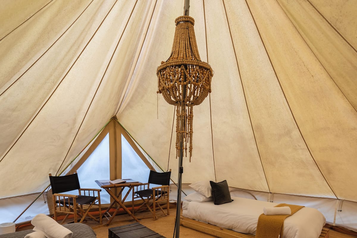 A tent with a bed, two chairs, a table, and a hanging light fixture.