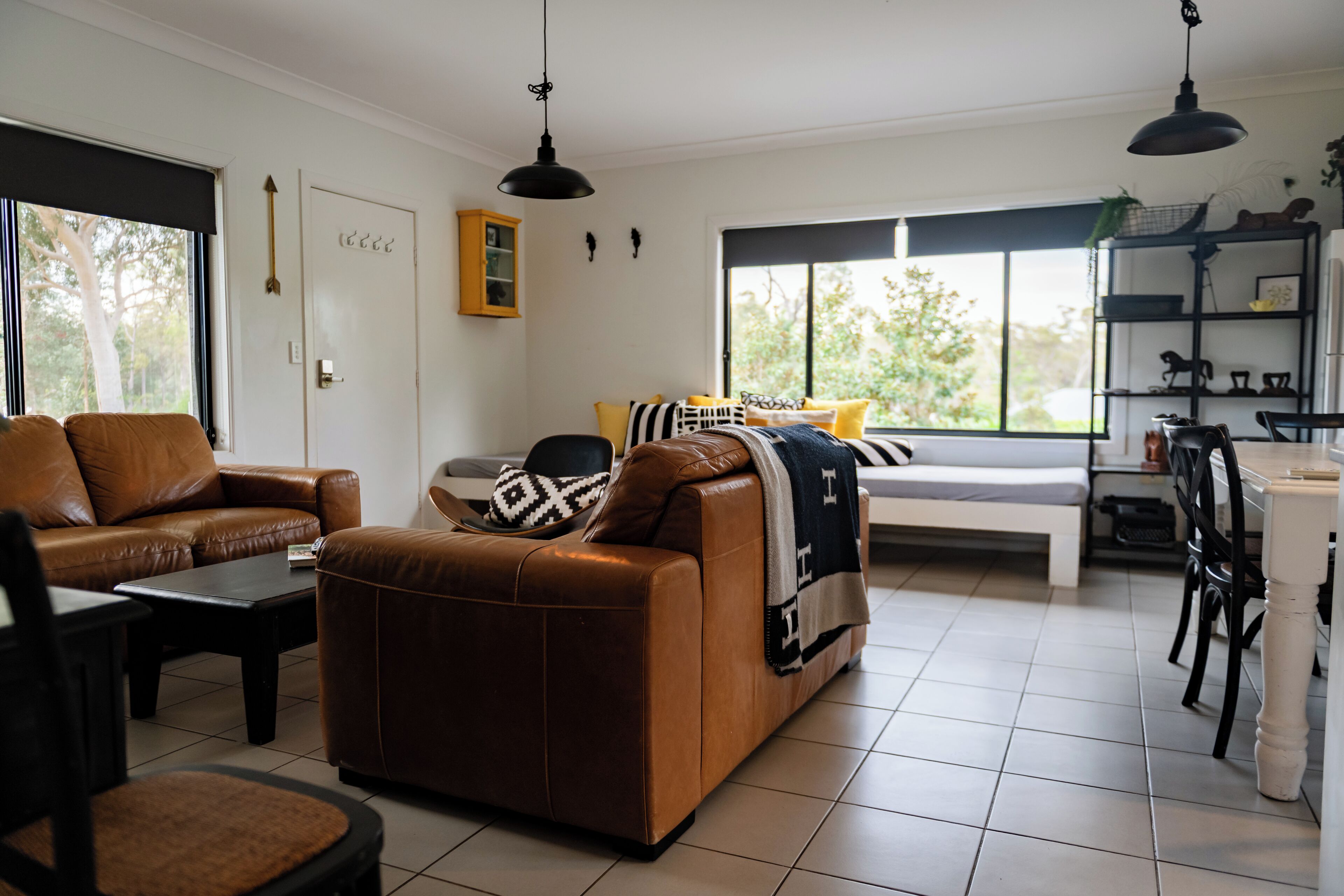 Un salon avec un canapé en cuir marron, une table basse et un coin repas comprenant une table et des chaises blanches.