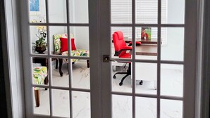 Ein Zimmer mit weißer Tür, einem Schreibtisch, einem roten Stuhl und einer Pflanze.