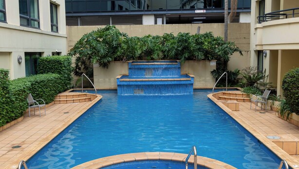 Una piscina rettangolare con una cascata al centro, circondata da una terrazza piastrellata e vasi con piante.