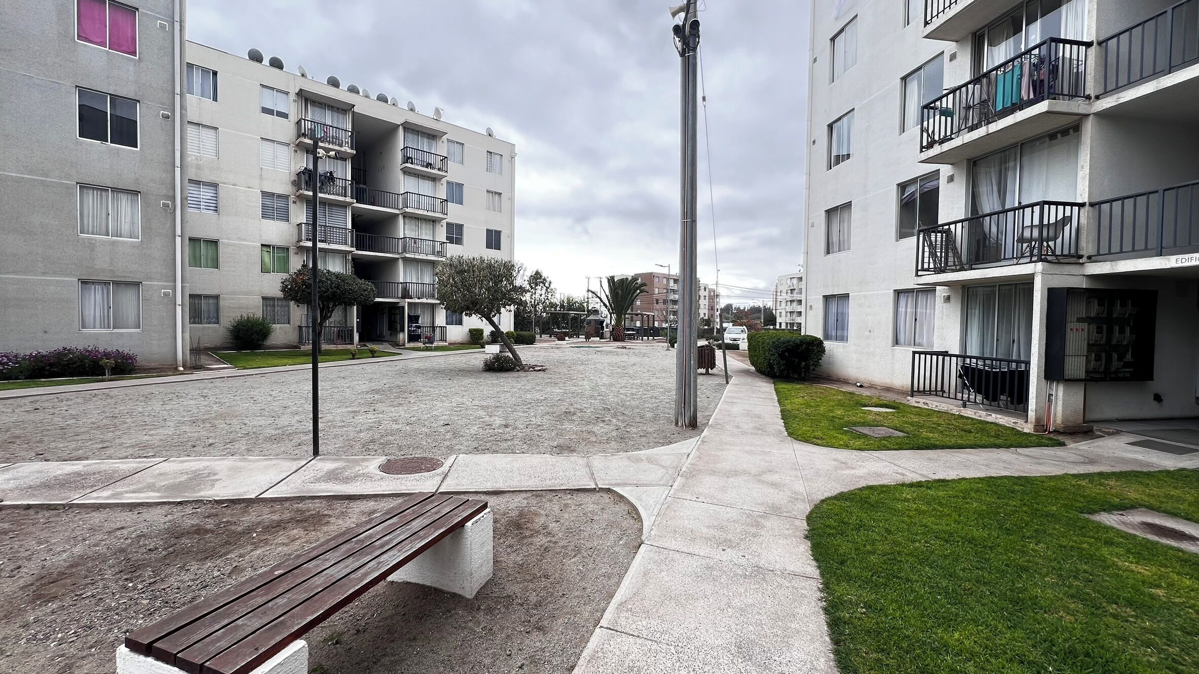 A residential building with multiple balconies, a central open space with a bench, and a small grassy area.