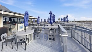 Terraza al aire libre con mesas y sillas, sombrillas azules y un letrero para un club de playa.