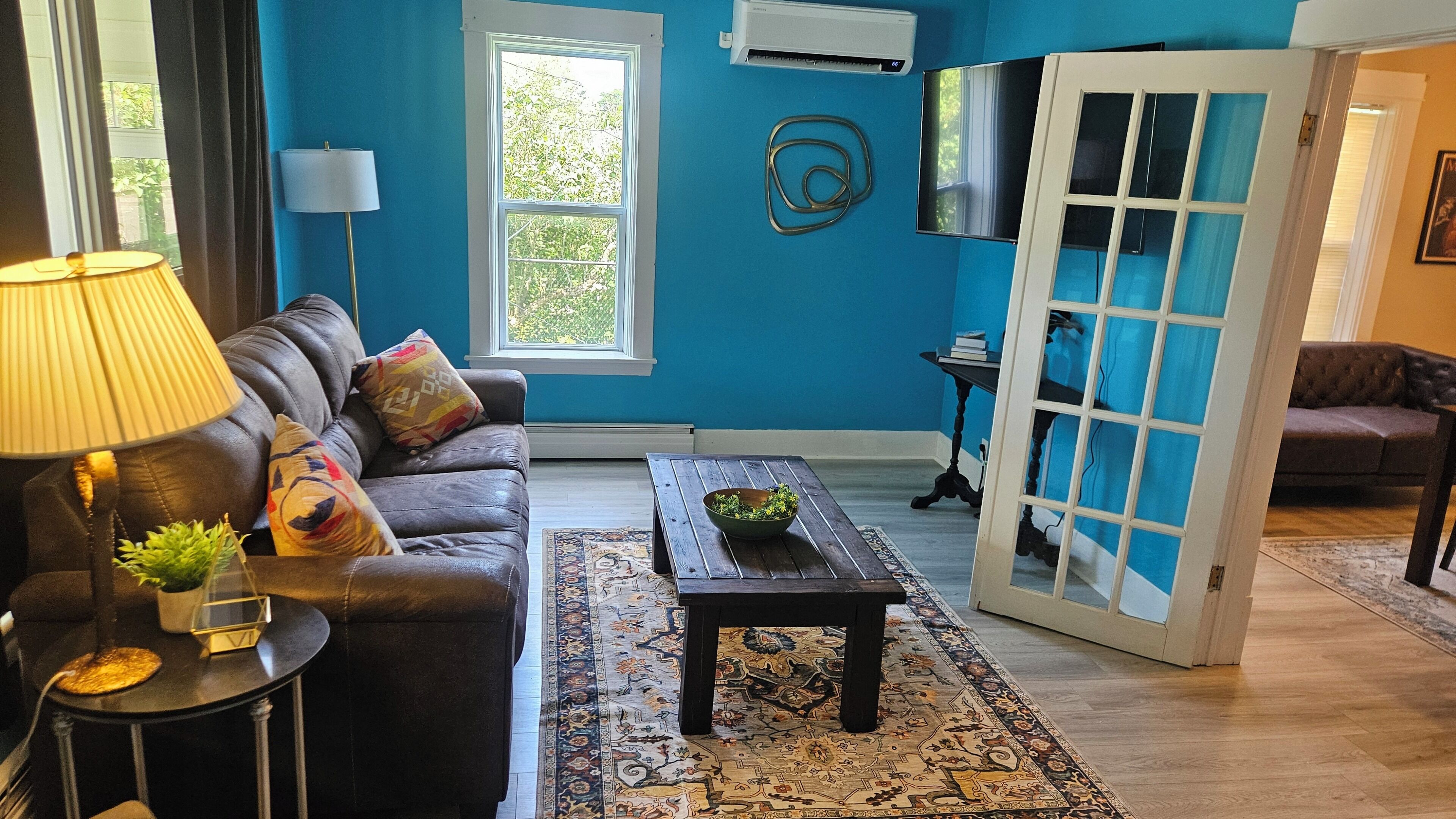 Un salon avec un mur bleu, un canapé, une table basse, une lampe et une porte donnant sur une autre pièce.