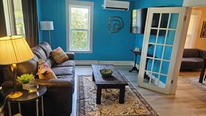 A living room with a blue wall, a sofa, a coffee table, a lamp, and a door leading to another room.
