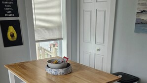 A kitchen with a wooden table, white cabinets, a window with blinds, and a door.