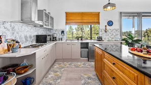 A modern kitchen with a wooden ceiling, large windows, and a view of greenery.