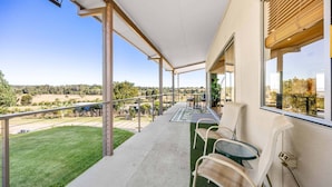 A balcony with a view of a green landscape, a table, and two chairs.