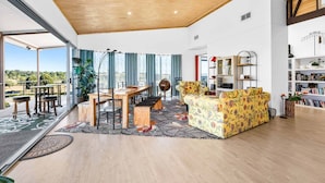 A spacious living area with a wooden ceiling, a dining set, a sofa, and a bookshelf.