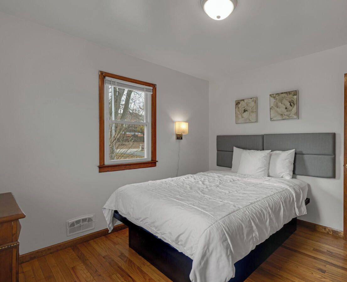 A bedroom with a bed, a window, a wall-mounted light, and three framed pictures.