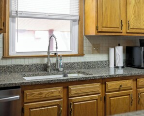 A kitchen with wooden cabinets, a granite countertop, a stainless steel sink, and a window with blinds. - Private 4 BDRM house, 5 Miles from Downtown #5 (Indianapolis)
