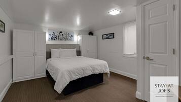 Une chambre à coucher avec un lit, des murs blancs et une porte. On y trouve des armoires et un luminaire au plafond.