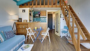 Ein gemütlicher Wohnbereich mit einer Holztreppe, einer Küche mit blauen Fliesen und einem Esstisch mit Stühlen.