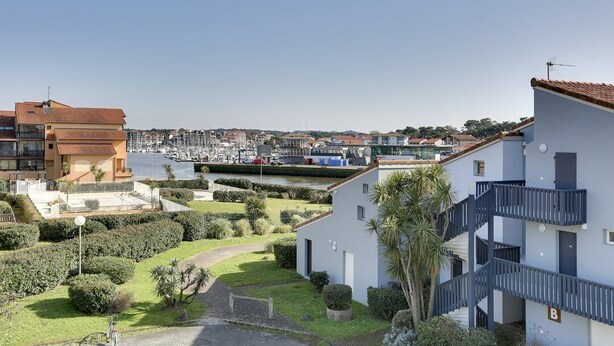 Ein Wohngebäude mit weißer Fassade und einem blauen Balkon, mit Blick auf eine Marina und Boote.