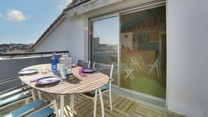 Ein Balkon mit einem runden Holztisch, Stühlen und einer Glastür zu einem Innenraum.