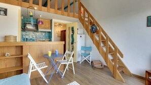 Ein gemütliches Zimmer mit einer Holztreppe, einer Küchenzeile mit blau gefliestem Fliesenspiegel und einem Essbereich mit einem kleinen Tisch und Stühlen.