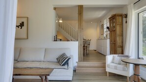 Ein geräumiger Wohnbereich mit einer Couch, einem Couchtisch und einem Esstisch. Eine Treppe führt zu einer oberen Ebene.