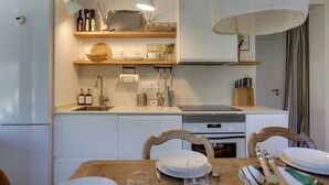 Eine kleine Küche mit weißen Geräten, Holzböden und einem Essbereich mit Tisch für zwei Personen.