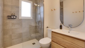 Ein modernes Badezimmer mit einer gläsernen Duschkabine, einer weißen Toilette und einem Holzausleger mit einem großen Spiegel.