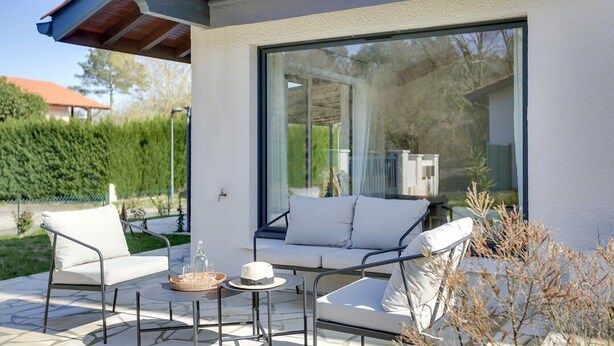 Eine Terrasse im Freien mit einer modernen Couch, zwei Sesseln, einem kleinen Tisch und einem Korb.
