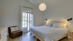 Ein Schlafzimmer mit einem Bett, einem Nachttisch, einer Kommode, einer Bank und einem Fenster mit Vorhängen.