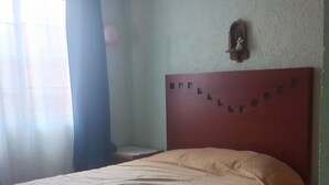 Une chambre à coucher avec un lit, une table de chevet, une horloge murale et une fenêtre avec des rideaux.