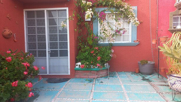 Un bâtiment rouge avec une fenêtre bleue, une porte blanche et un patio carrelé agrémenté de plantes en pot.
