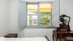 A bedroom with a bed, a nightstand, a wooden dresser, and a window with a view of greenery outside.