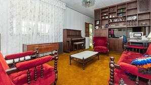 A living room with a piano, red armchairs, a coffee table, and a bookshelf.