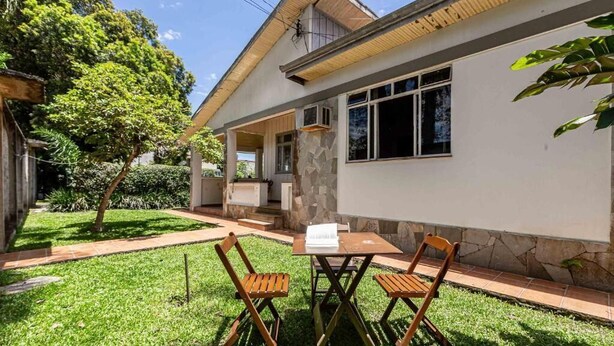 A house with a covered porch, a small lawn, and two wooden chairs.