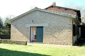 Ein Steinhaus mit einer grünen Tür, einem kleinen Anbau und einer gepflasterten Fläche davor.