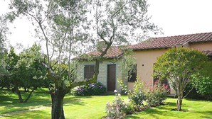 Una casa con techo de tejas, fachada de ladrillo y un césped cuidado con árboles y flores.