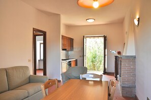 A dining area with a wooden table and chairs, a sofa, a kitchen in the background, and a view through a glass door. - Villa i Noccioli   18 sleeps, swimmingpool, estate (CAPRANICA)