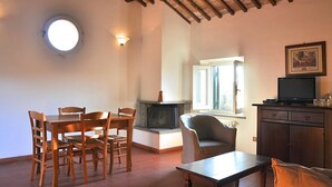 Una habitación con chimenea, un tragaluz circular, un televisor sobre un mueble bajo y un comedor con mobiliario de madera.