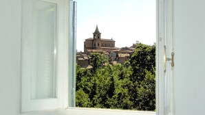 Una ventana con vistas a un edificio histórico con un campanario, rodeado de vegetación.