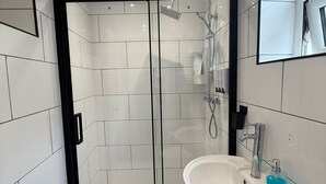 Une salle de bain moderne avec des murs recouverts de carreaux blancs, une douche en verre, un lavabo blanc avec un distributeur de savon et un tapis rouge.