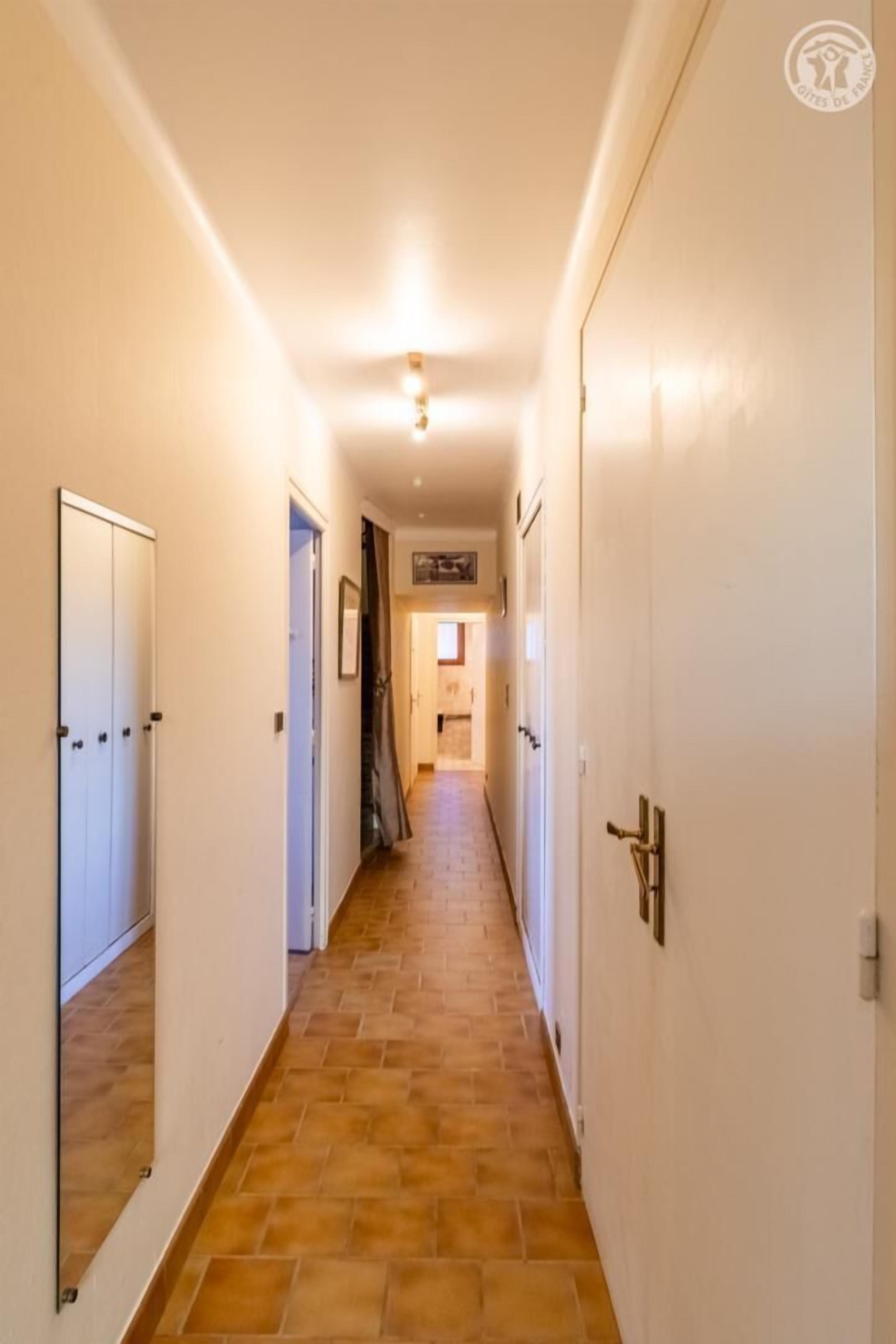 Ein Flur mit weißen Wänden und Holzboden, der zu einem Zimmer mit Bett und Fenster führt.