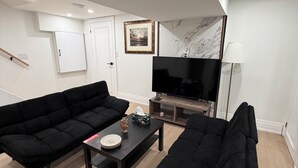 Una sala de estar moderna con dos sofás negros, una mesa de centro, un televisor de pantalla plana y una pared de mármol.