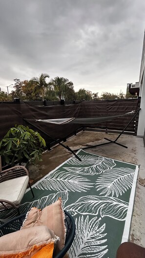Eine Dachterrasse mit einer Hängematte, einer gemusterten Matte und einem Stuhl.